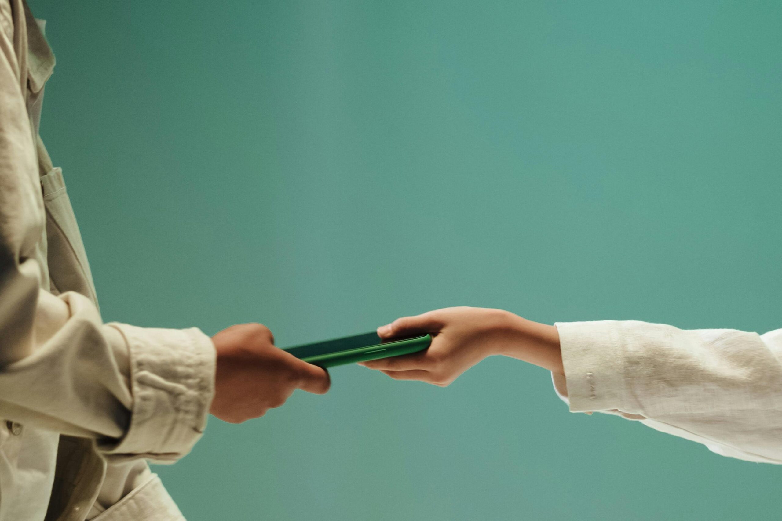 Two people exchanging a green mobile phone against a solid green background.